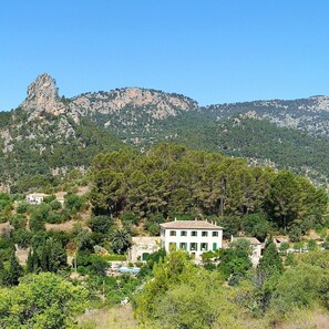 A building with a white facade and green shutters, surrounded by lush greenery and mountains in the background. - Finca sa Màniga (Bunyola)