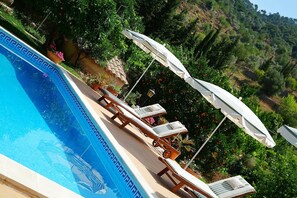 Une piscine entourée de verdure et de collines, avec des chaises longues et des parasols.