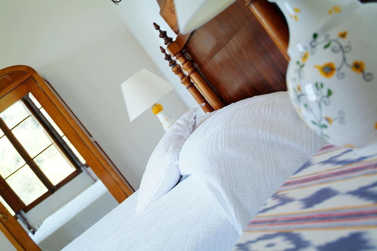 Un dormitorio con cabecera de madera, edredón blanco y ventana con vista a la vegetación.