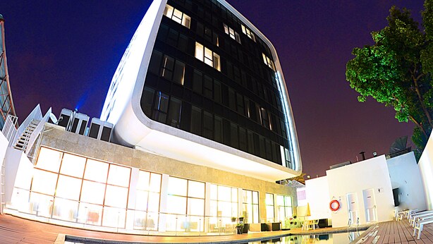 A modern building with a reflective pool in front, large windows, and a tree to the right. - Hotel Ekuikui I (Huambo)
