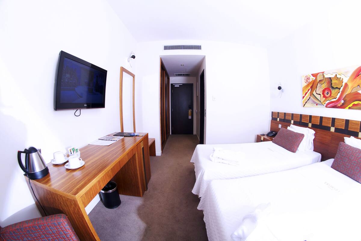 Ein Hotelzimmer mit einem Holztisch, zwei Betten, einem Fernseher und einem Bild an der Wand.