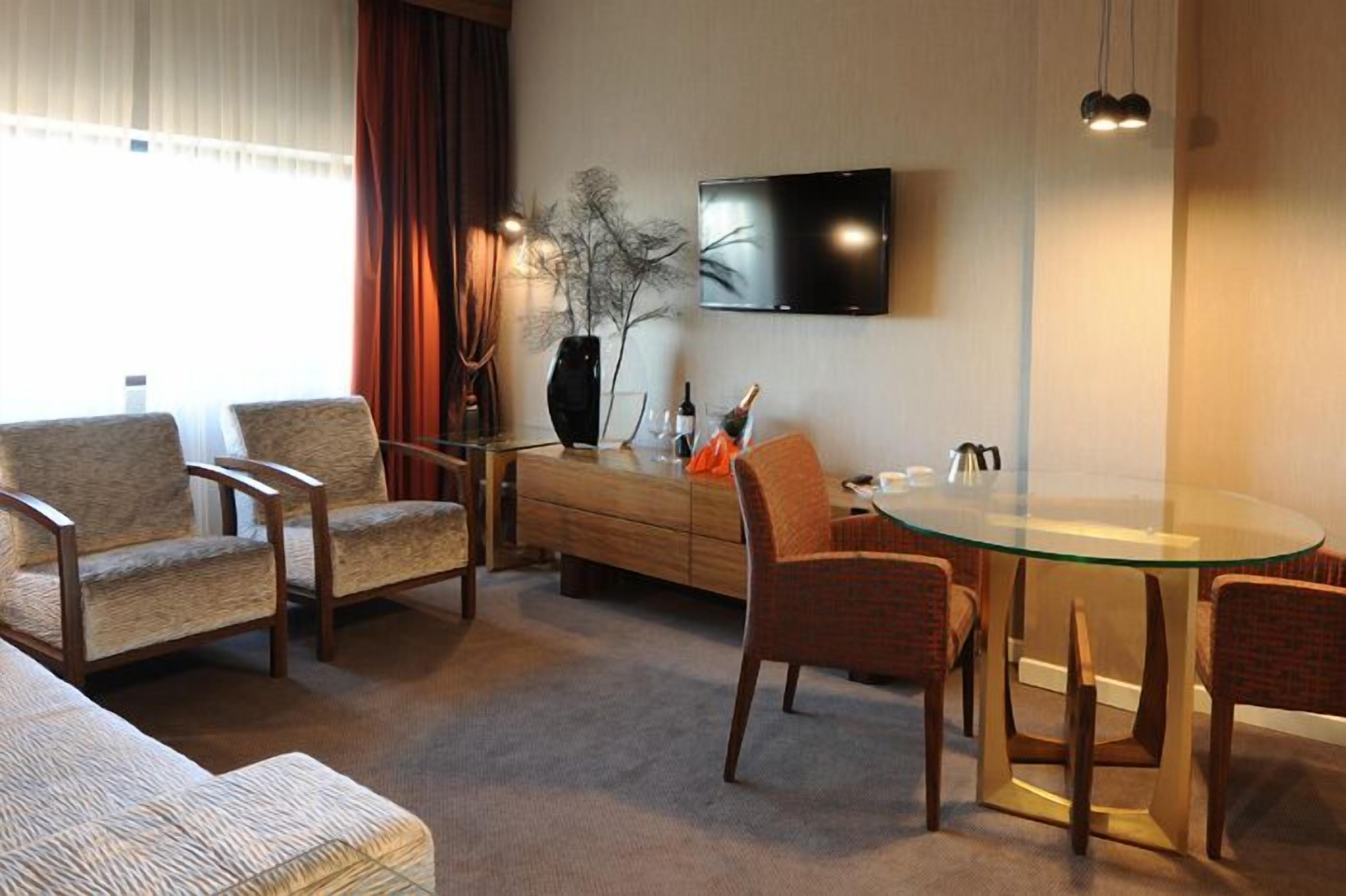 Een moderne woonkamer met een eettafel met glazen blad, twee banken, een salontafel en een flatscreen televisie aan de muur.