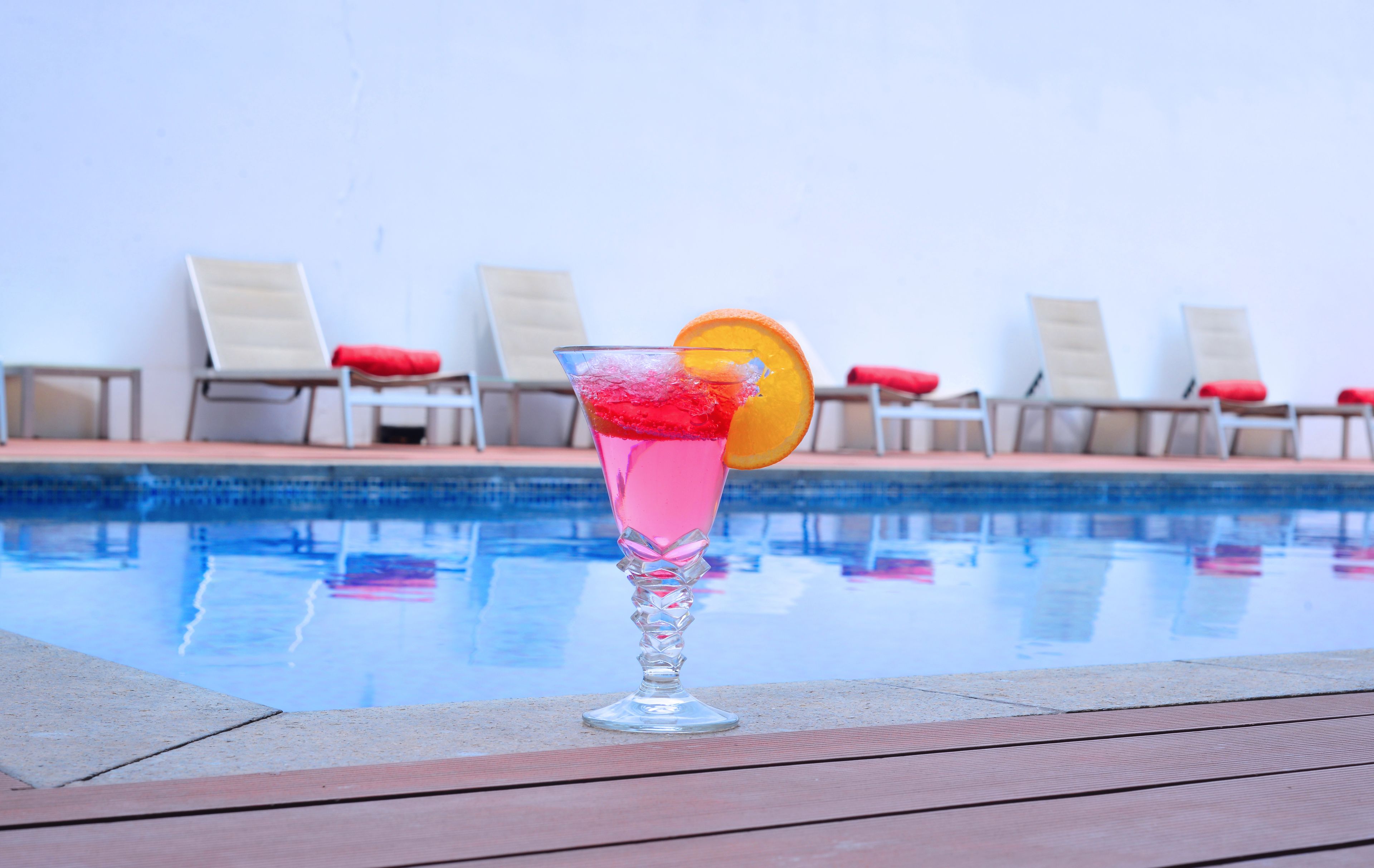 A poolside setting with lounge chairs and a drink in a glass.