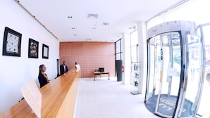 A reception area with a wooden reception desk, framed artwork on the walls, a bench, and a revolving door. - Hotel Ekuikui I (Huambo)