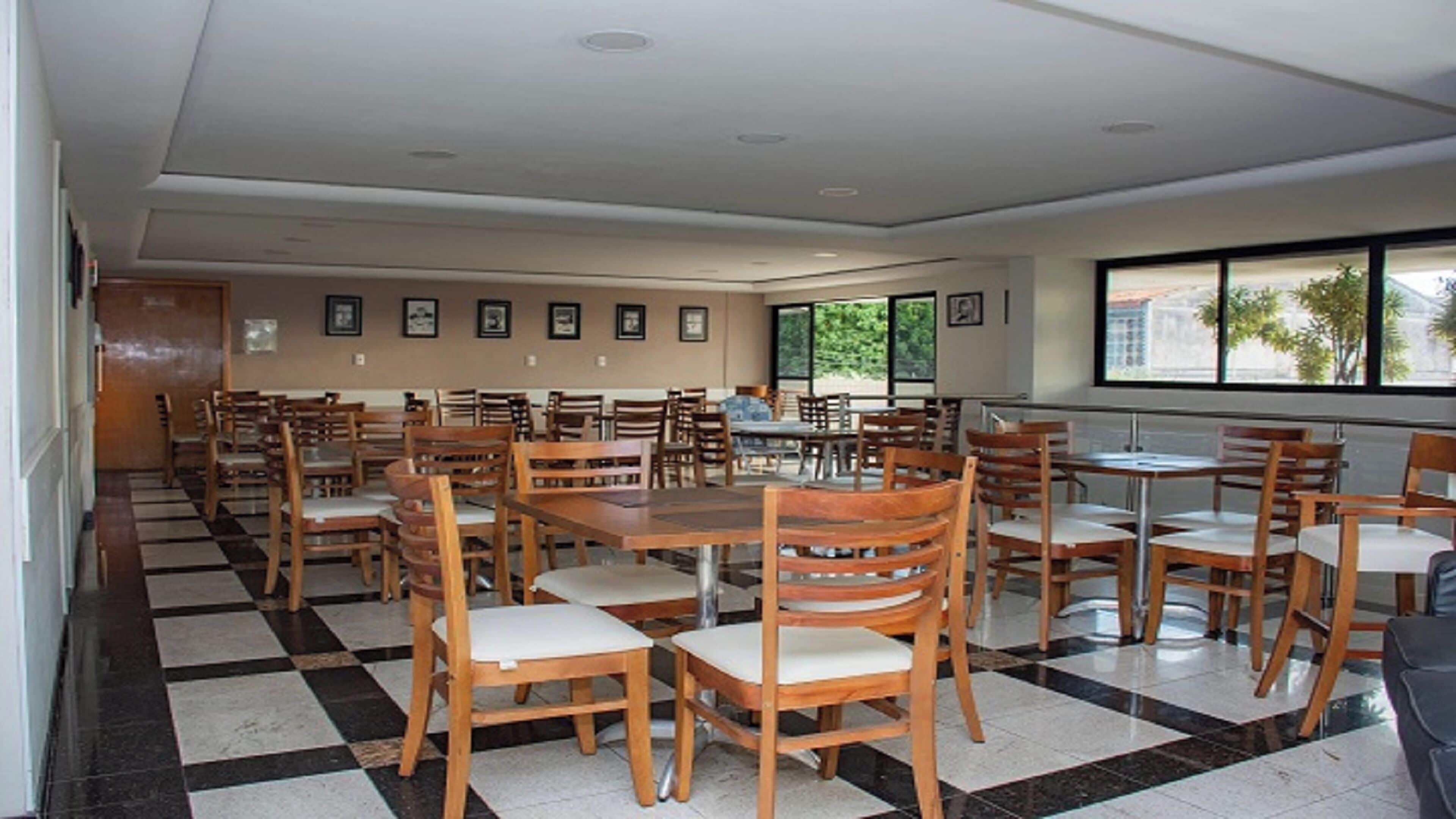 A dining area with multiple wooden tables and chairs, a checkered floor, and framed pictures on the walls.