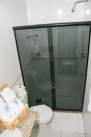 Un box de ducha con paredes y puerta de cristal, un inodoro blanco y una cesta de mimbre con toallas.