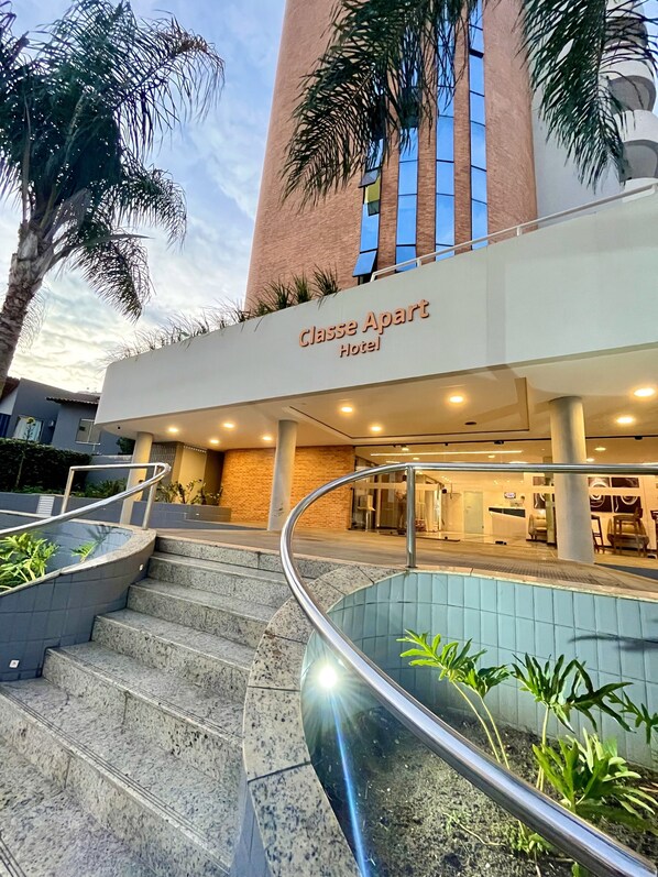 Exterior del Clase Apart Hotel con zona de piscina, escaleras y palmeras.