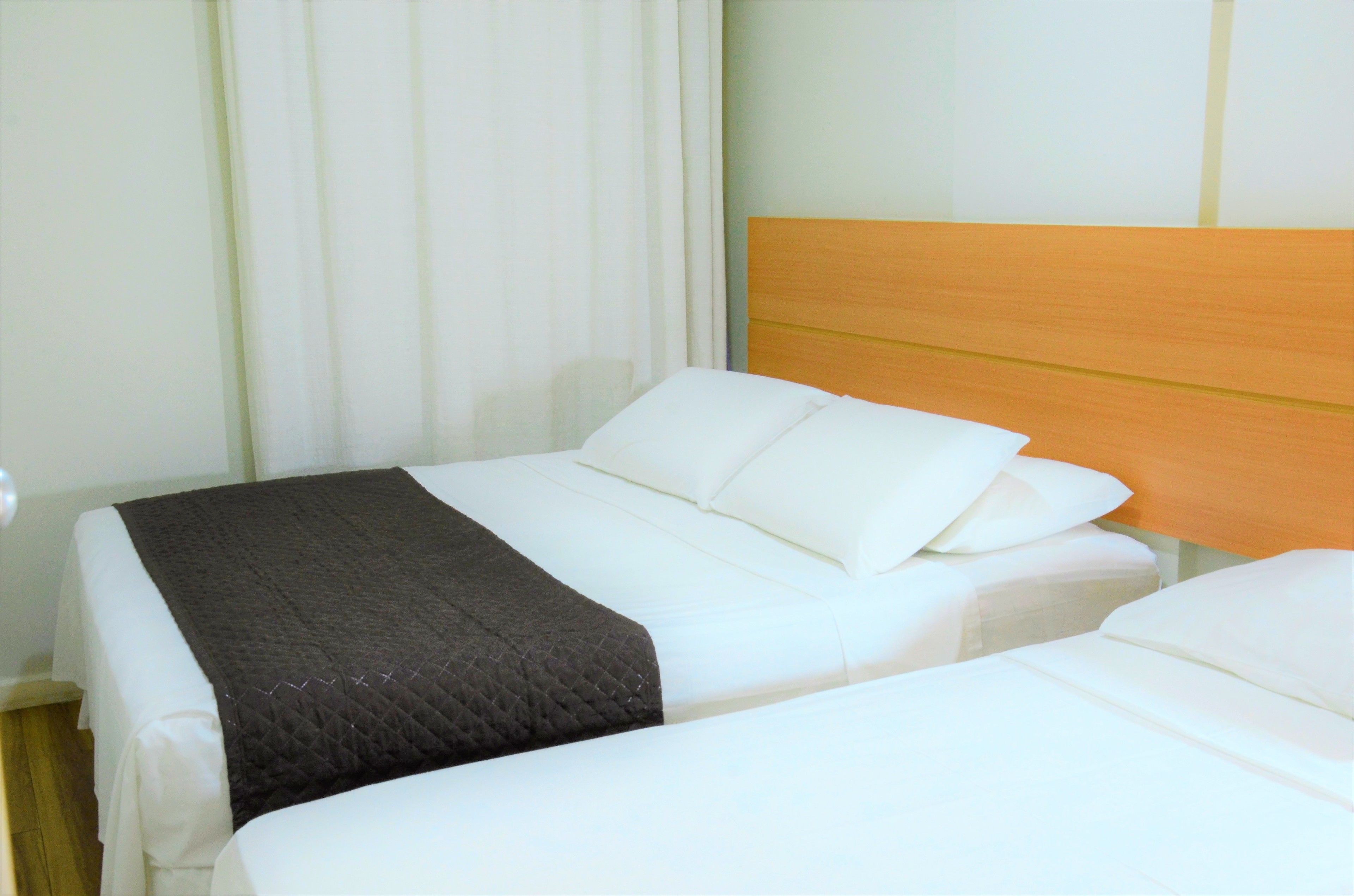 Habitación de hotel con dos camas, cabecero de madera y ropa de cama blanca.
