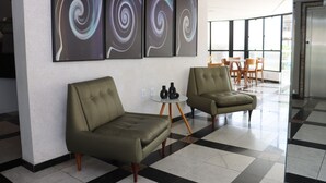 Un hall d’entrée moderne avec deux canapés verts, une petite table ronde et trois tableaux abstraits accrochés au mur.