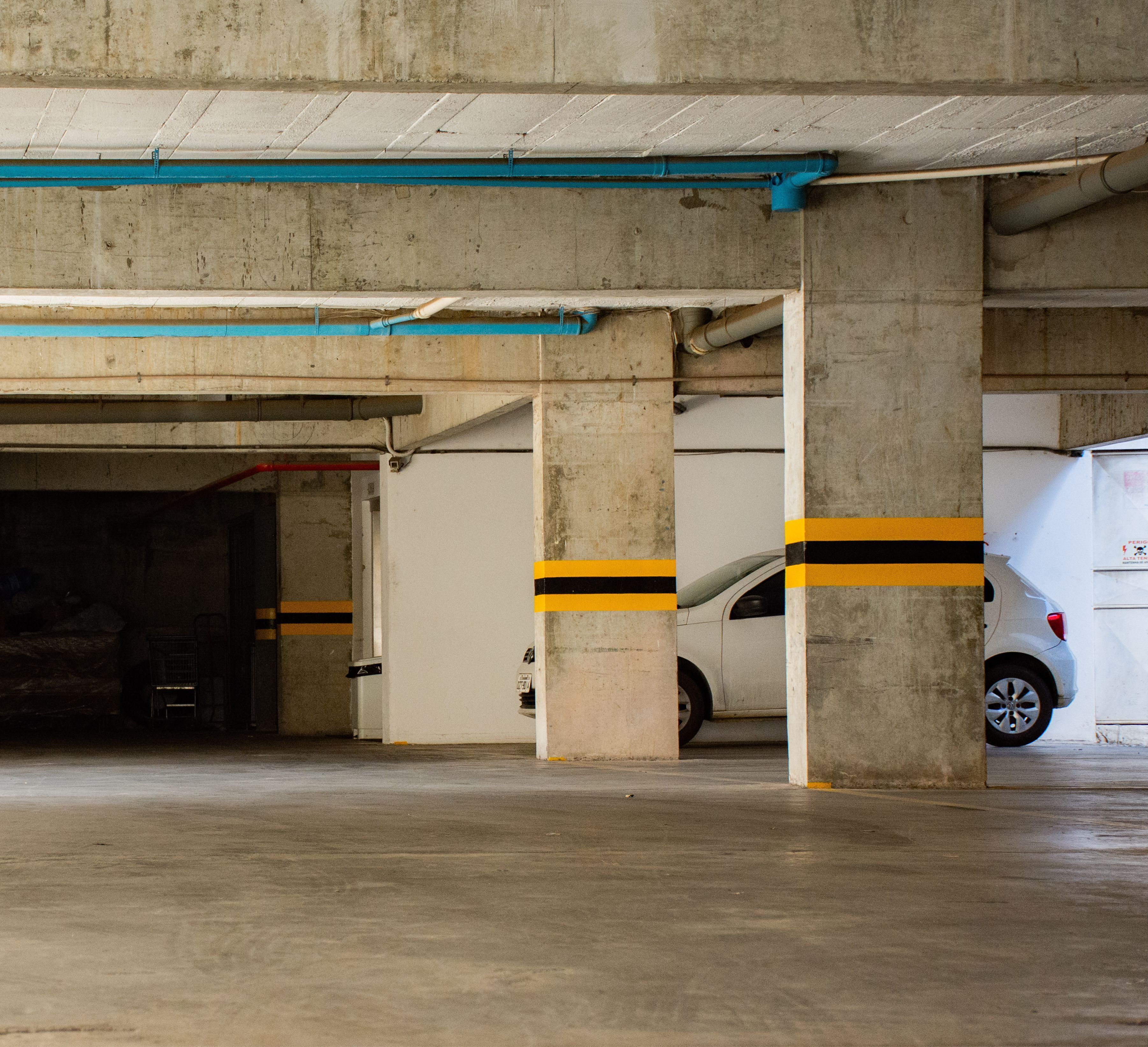Uma garagem subterrânea com pilares de concreto, um carro branco e uma van branca.