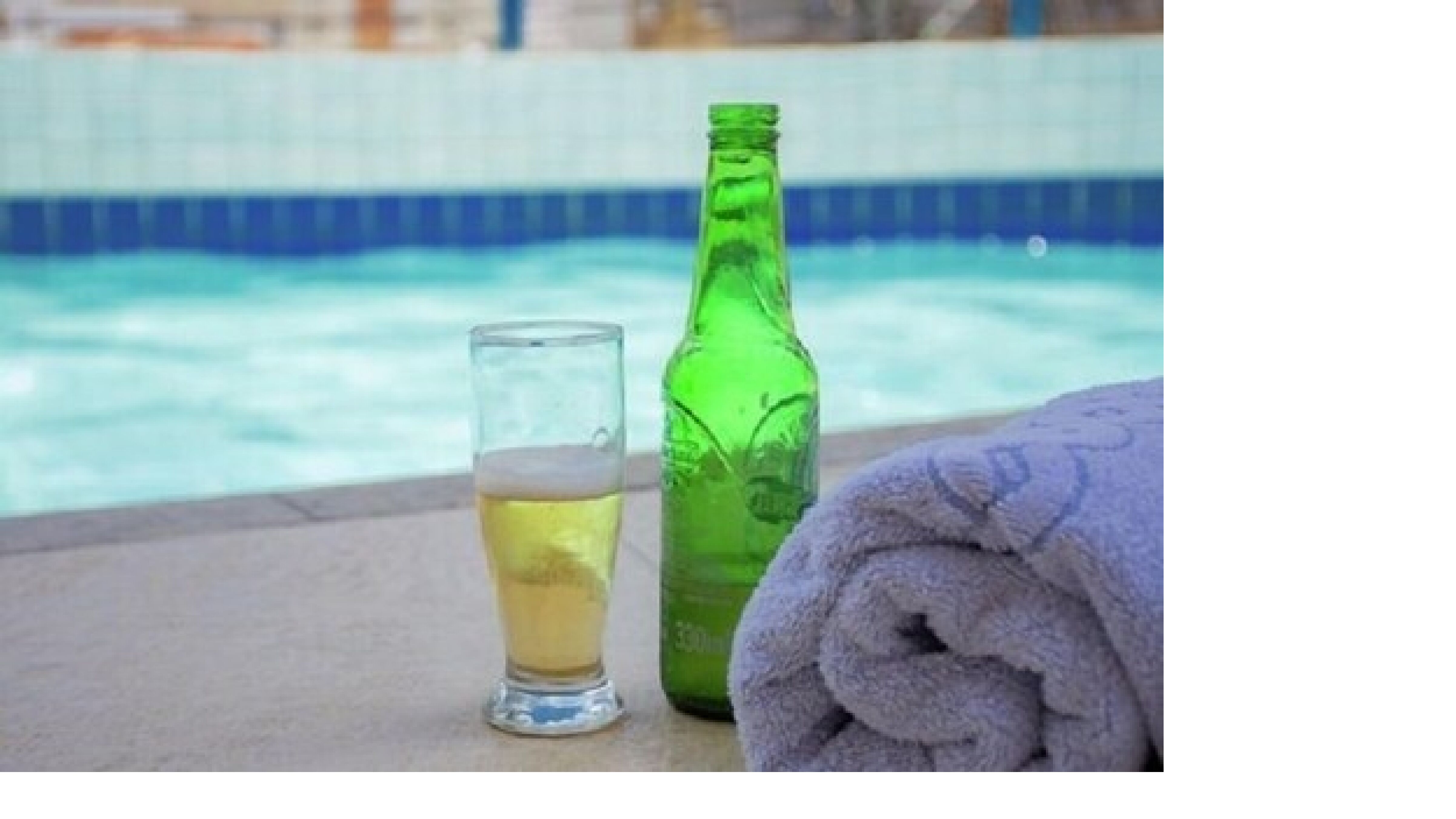 Una cerveza y una botella verde junto a una piscina.
