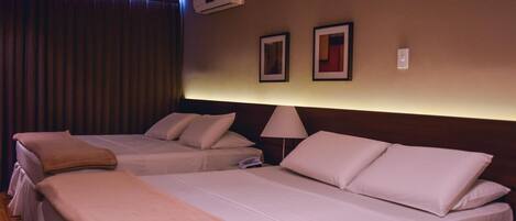 A hotel room with two beds, a bedside lamp, an air conditioning unit, and two framed pictures on the wall.