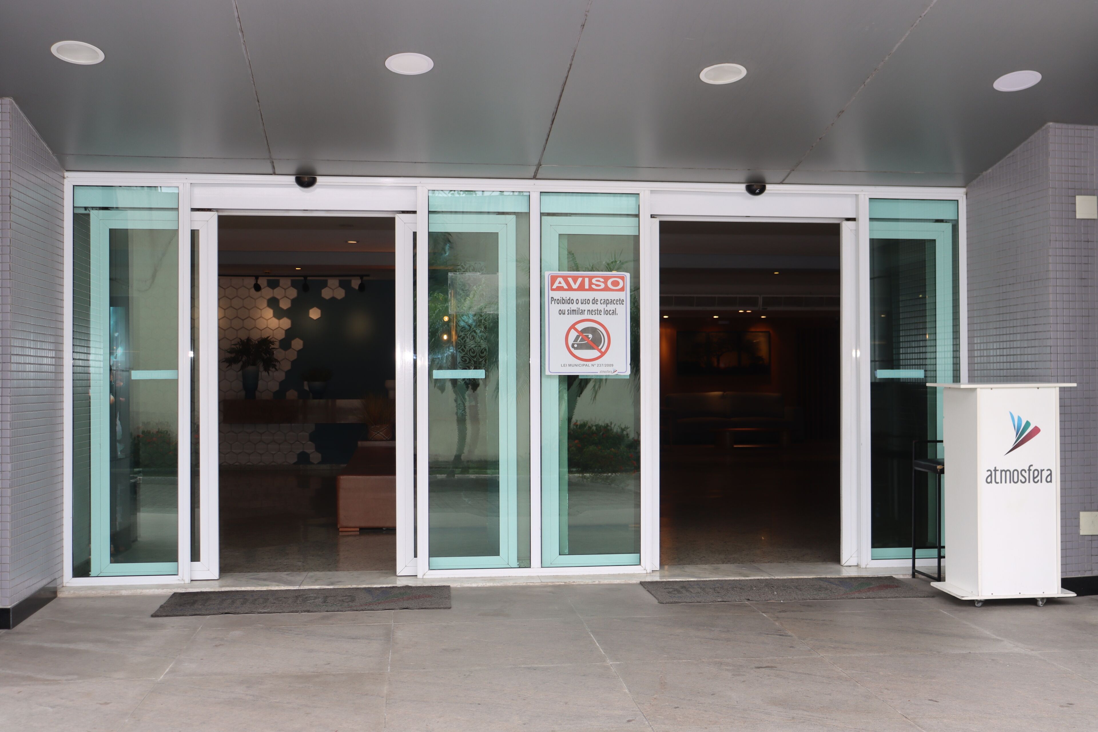 Entrada de un hotel con puertas de cristal, un cartel que prohíbe estacionar y un mostrador de recepción.