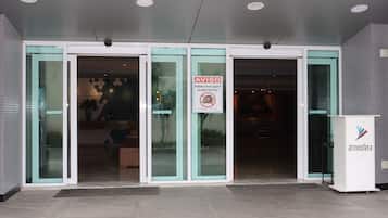 Entrada de un hotel con puertas de cristal, un cartel que prohíbe estacionar y un mostrador de recepción.
