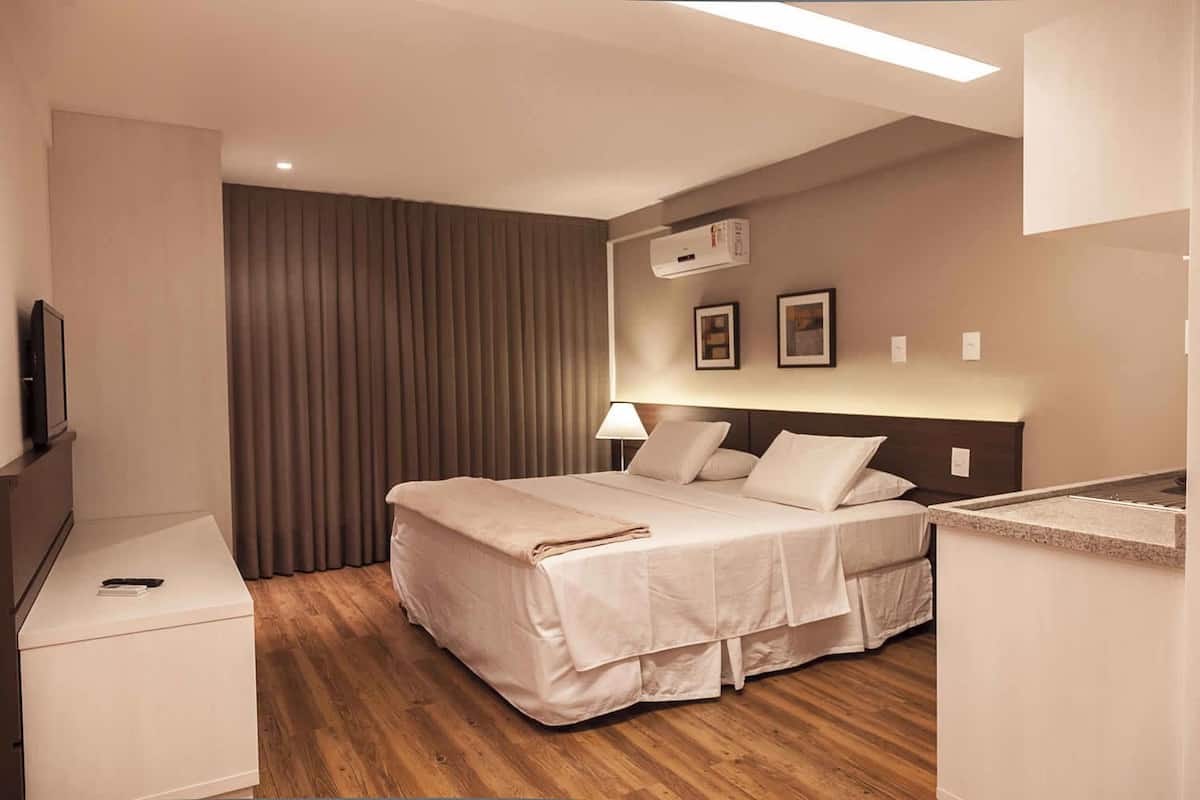 A hotel room with a bed, bedside table, lamp, and a TV on a stand.