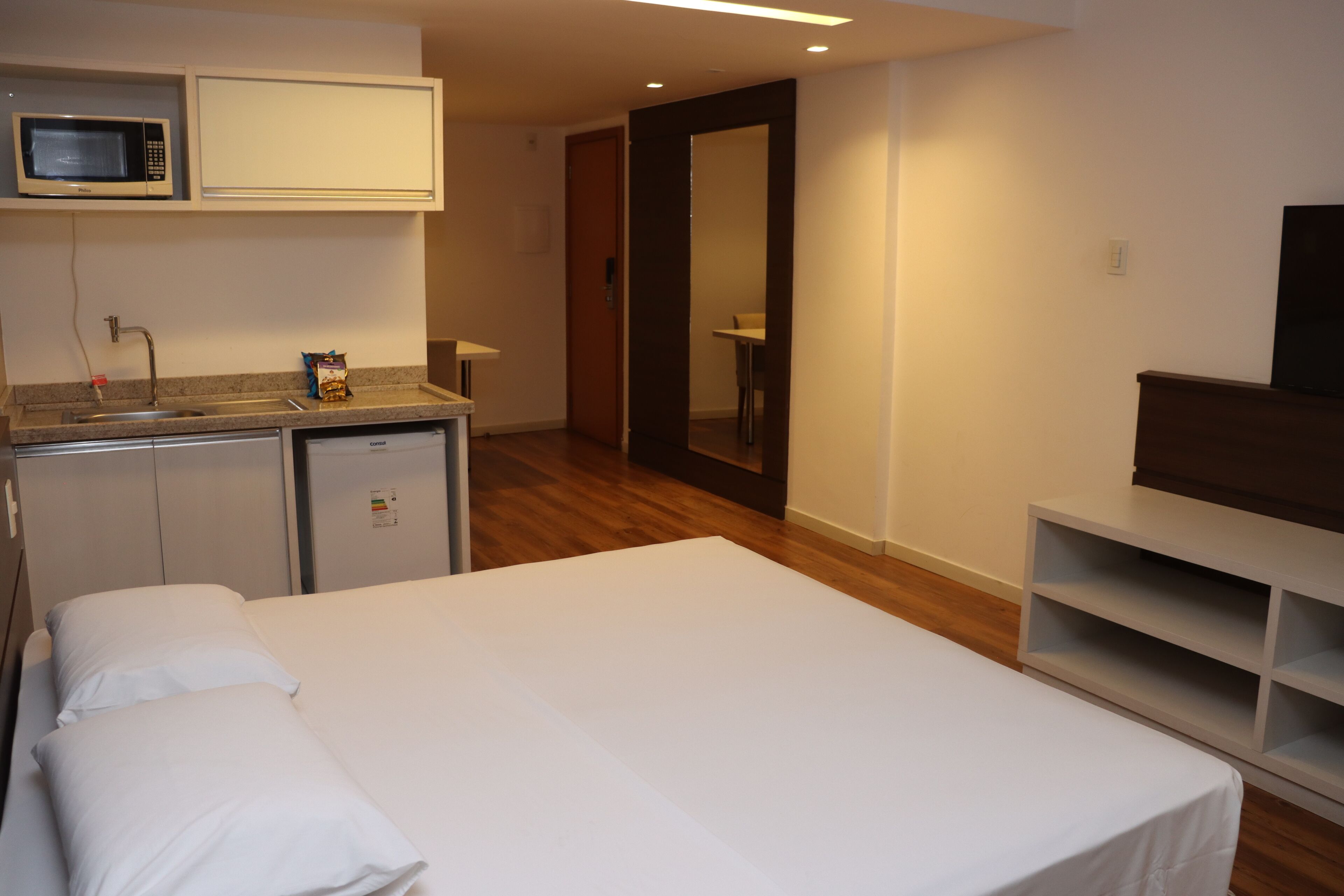A hotel room with a bed, a small kitchenette with a microwave, a sink, and a TV.