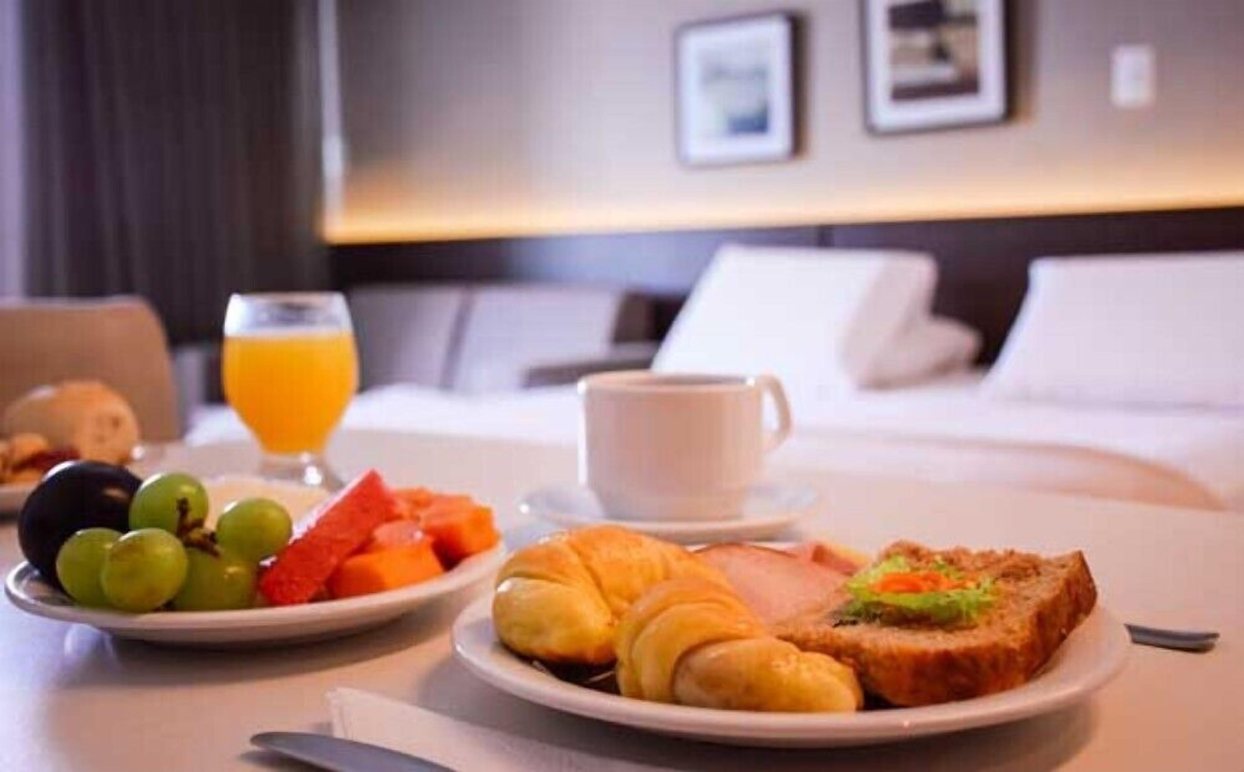 A breakfast setup with croissants, toast, fruit, and a glass of orange juice on a hotel room table.