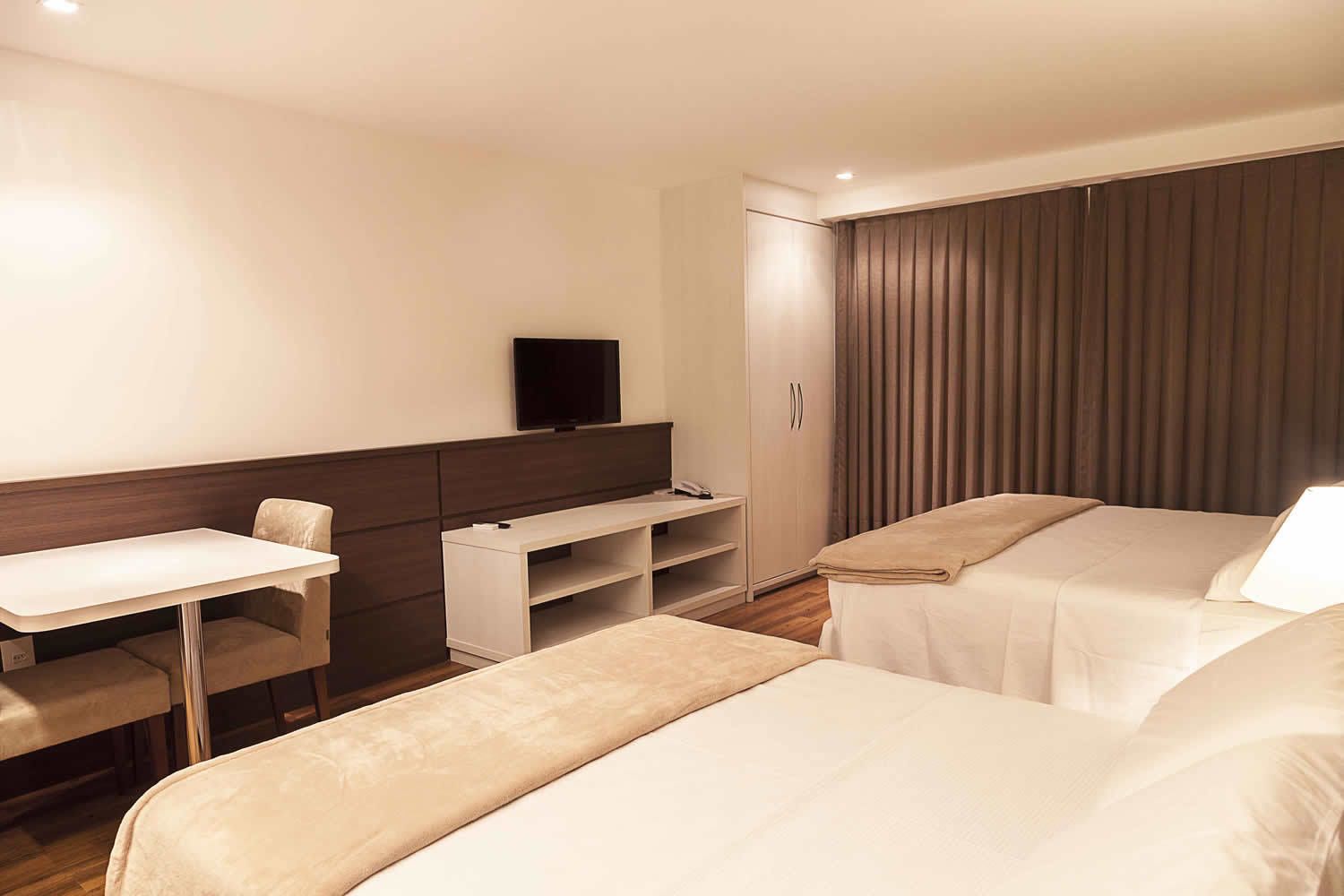 A hotel room with two beds, a desk, a television, and a wardrobe.