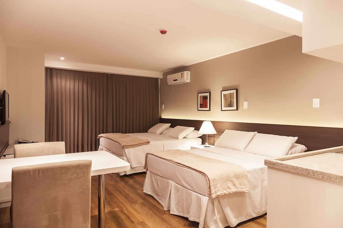 A hotel room with two beds, a desk, a TV, and a window with curtains.