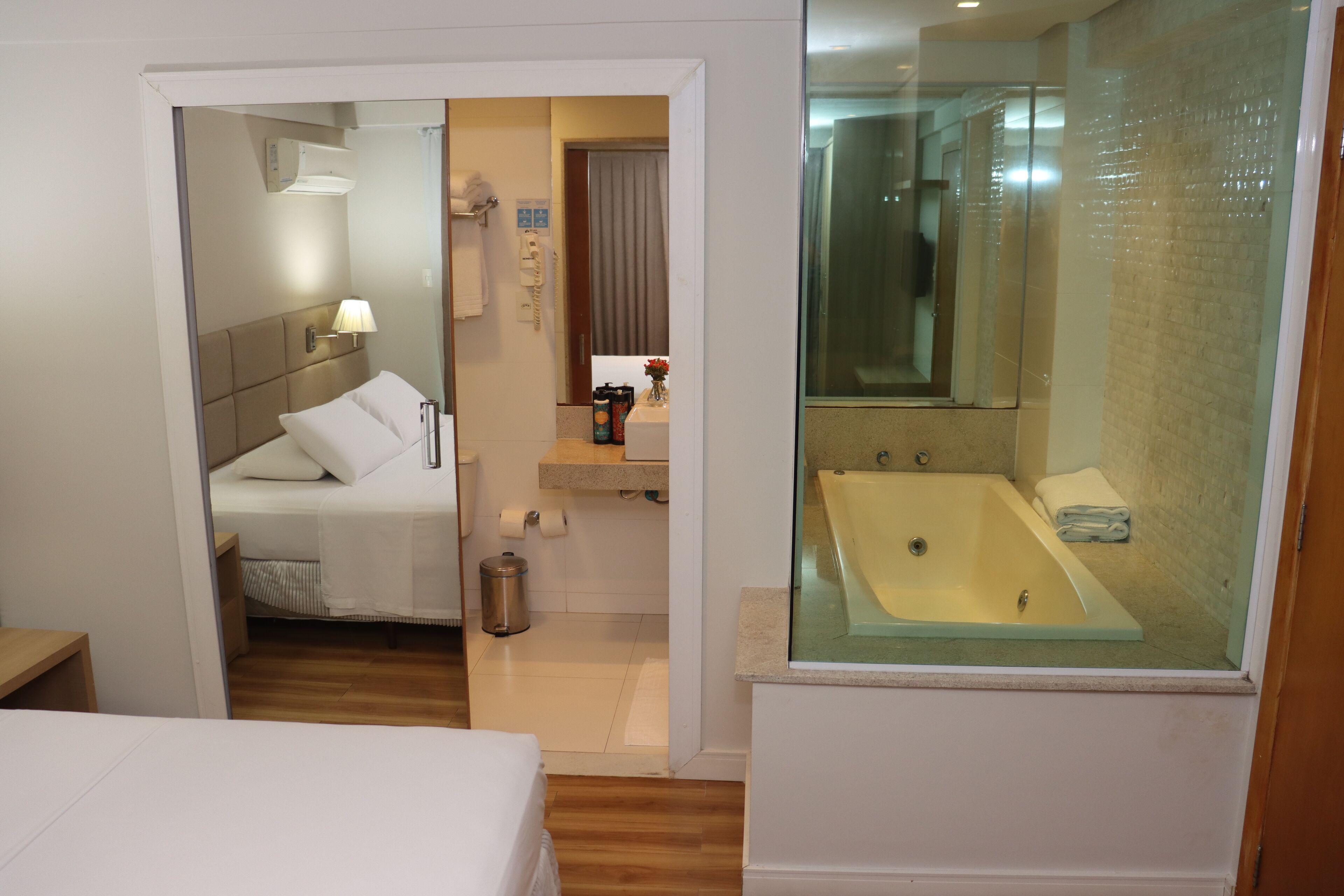 A hotel room with a bed, a bathroom with a bathtub, and a mirror.