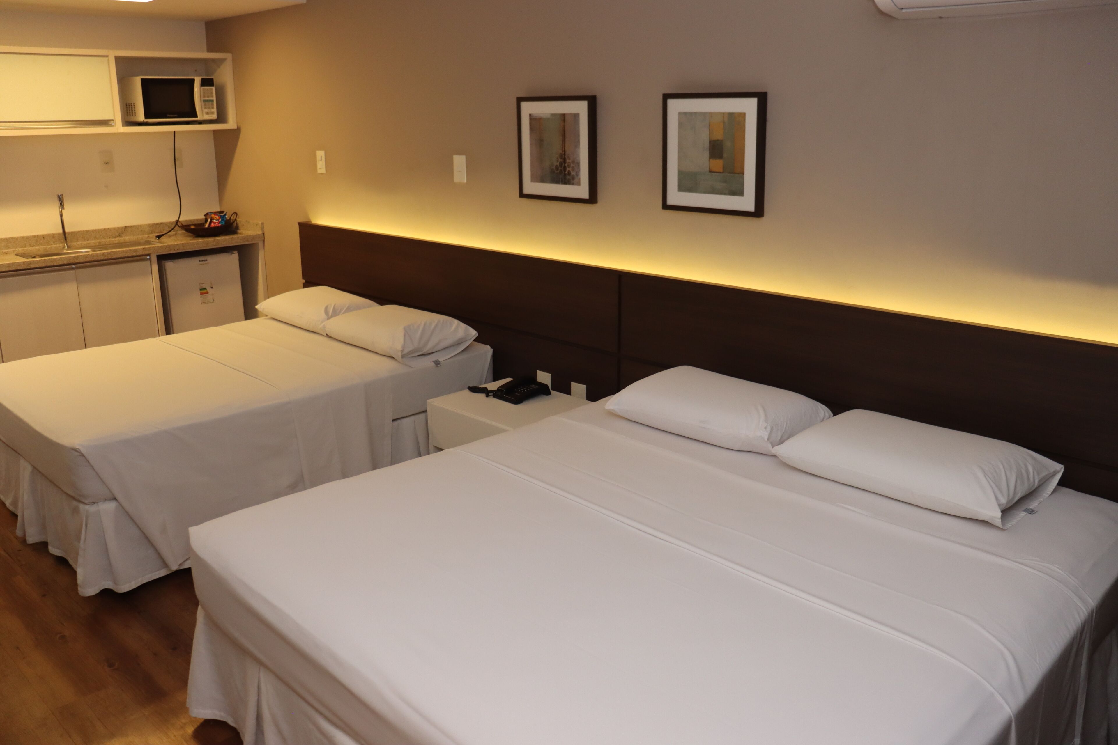 A hotel room with two single beds, a small kitchenette, and a microwave.