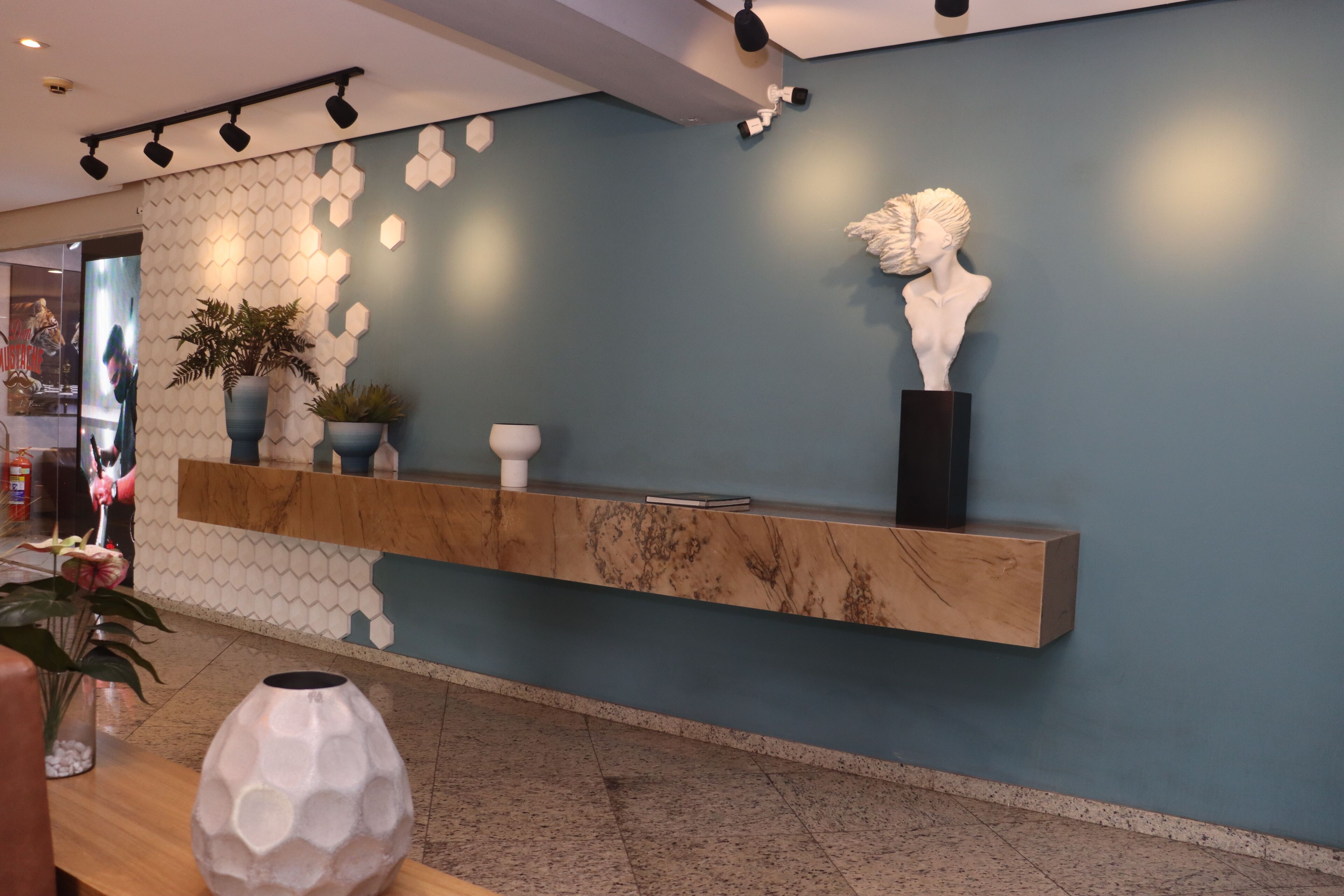 Una zona de recepción con mostrador de mármol, plantas en macetas y un busto.