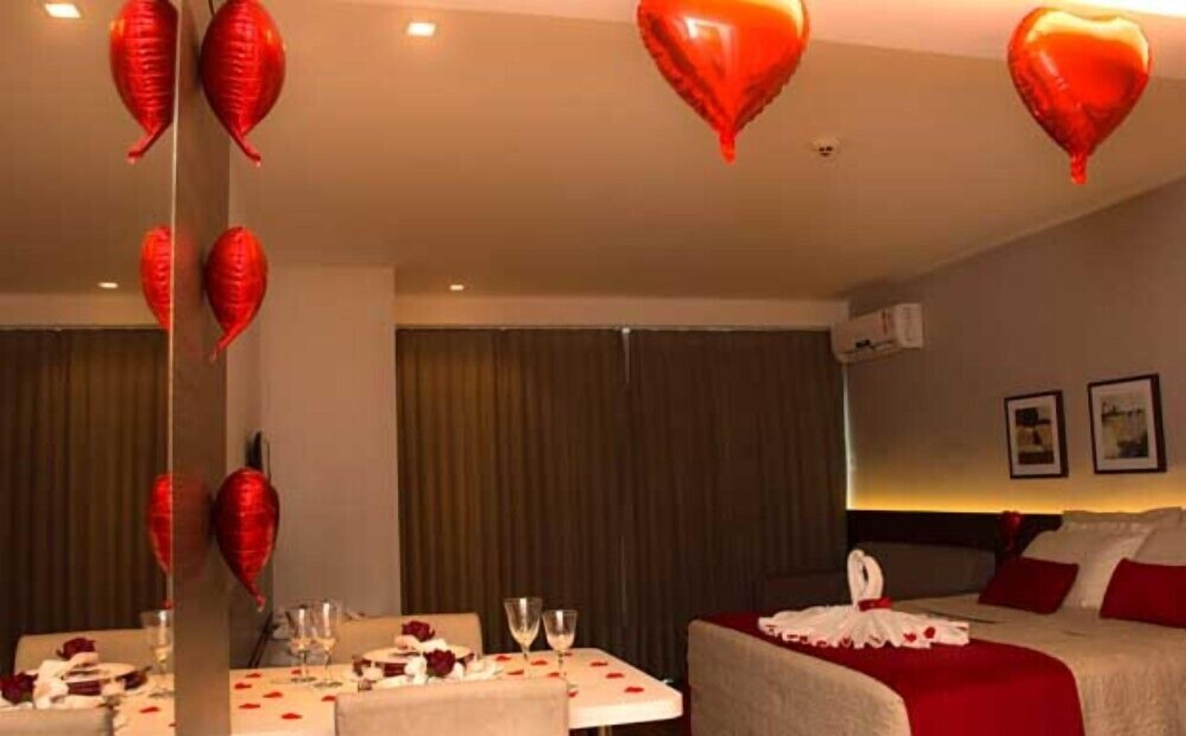 A hotel room with a bed, a table set with a bouquet of flowers, and heart-shaped decorations on the ceiling.