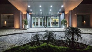Una entrada de hotel con diseño moderno, que presenta un acceso por puerta de vidrio, plantas en macetas y un camino de adoquines que conduce a la entrada.