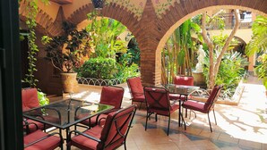 A patio area with red cushioned chairs and a glass table, surrounded by potted plants and a brick archway. - Hotel Casa La Gran Senora (Tequila)