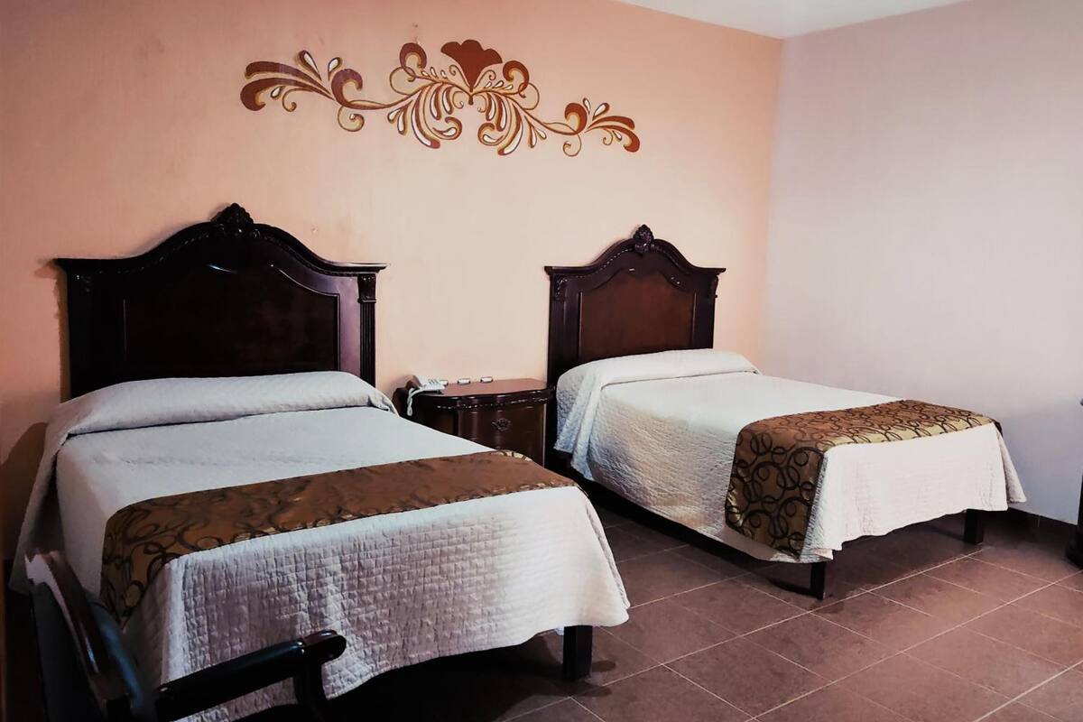 Dos camas individuales con cabeceras de madera, una mesita de noche con teléfono y un adorno decorativo sobre las camas.