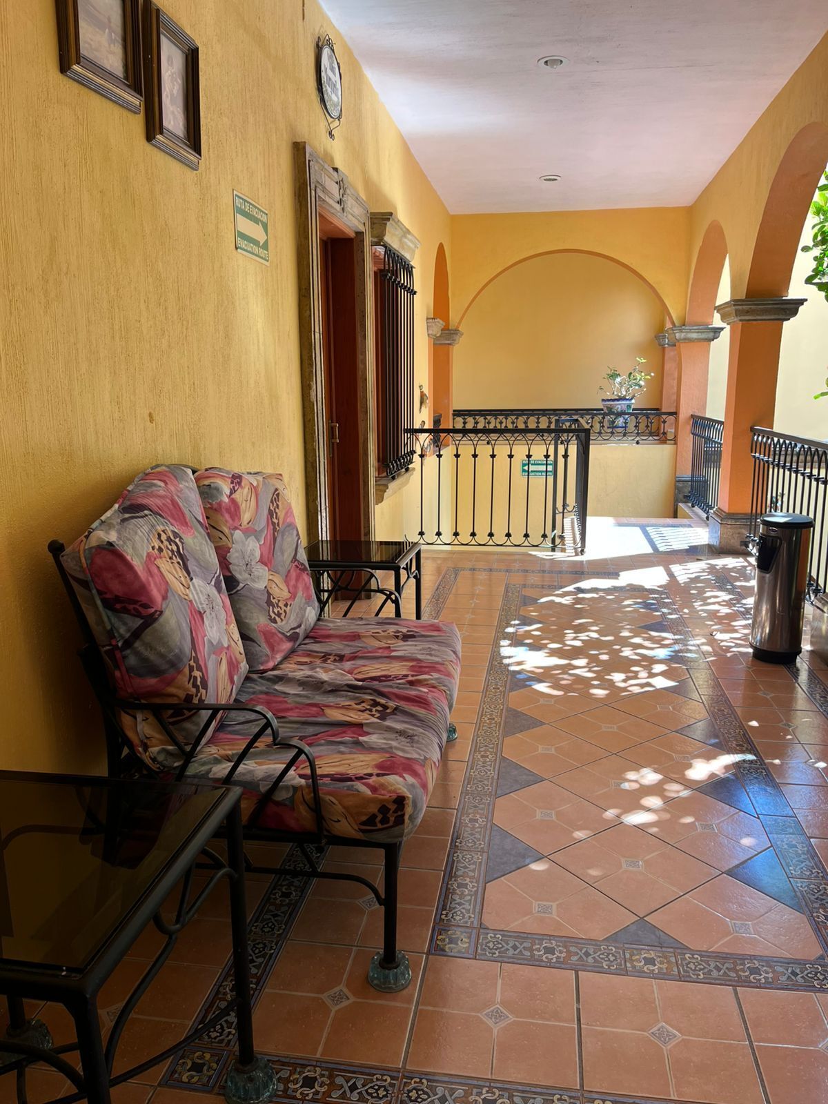 A sunlit corridor with a sofa, a trash can, and a railing.