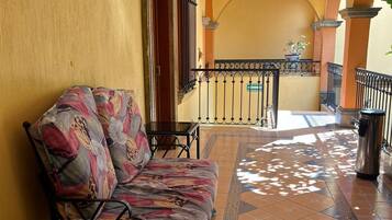 A sunlit corridor with a sofa, a trash can, and a railing.