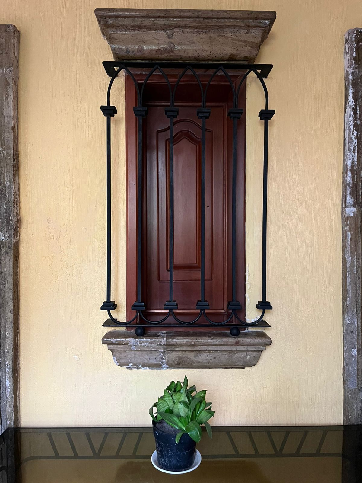 Una ventana con una reja de hierro forjado, una puerta de madera y una planta en maceta sobre una mesa.