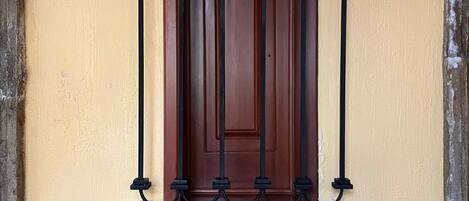 Una ventana con una reja de hierro forjado, una puerta de madera y una planta en maceta sobre una mesa.