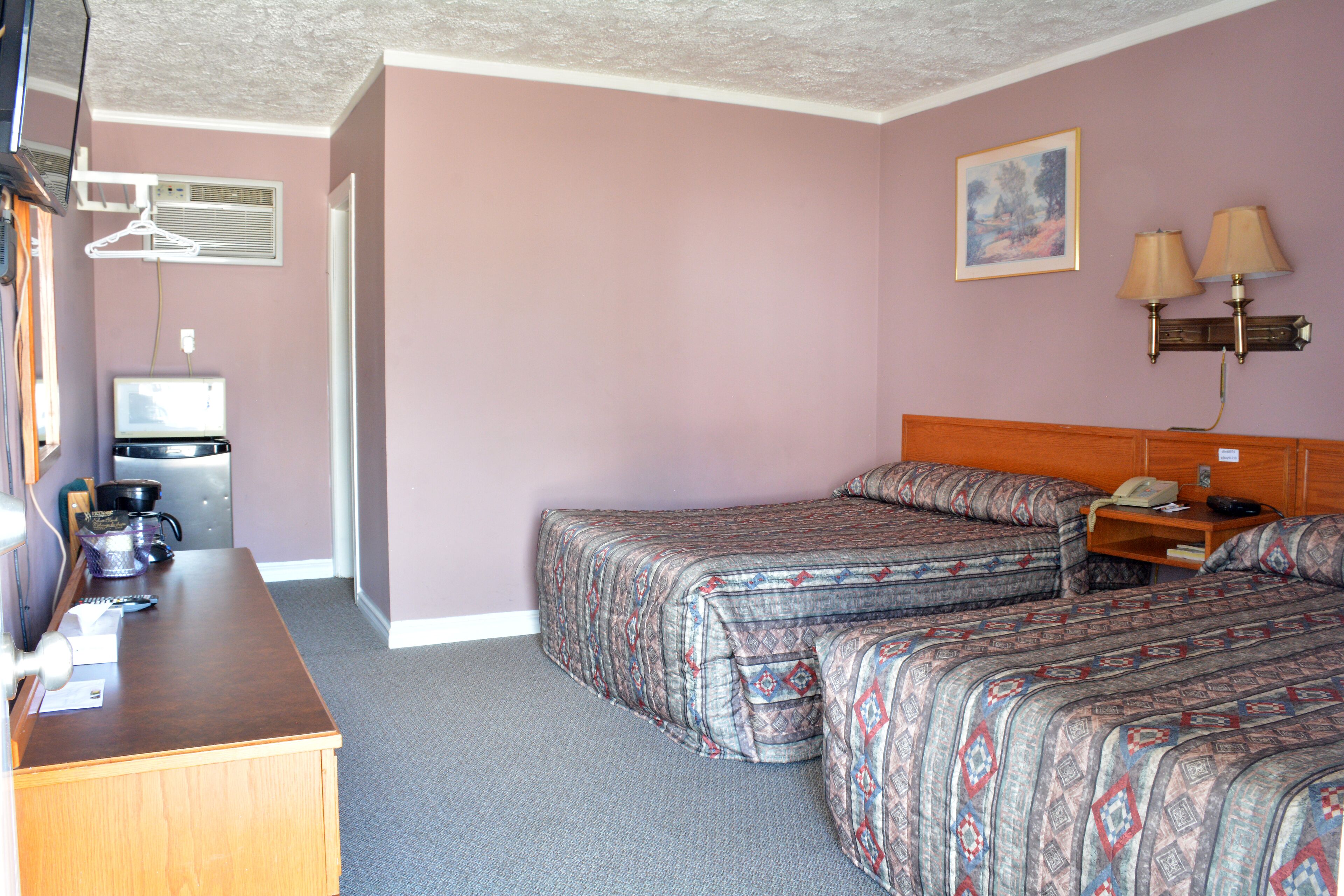 Una habitación de hotel con dos camas, un escritorio, una kitchenette y un cuadro en la pared.