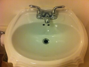 A white pedestal bidet with a single faucet and a drain.