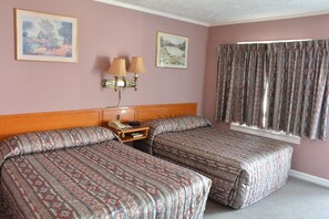 A hotel room with two beds, a wooden headboard, a nightstand, two wall-mounted lamps, and two framed pictures on the wall.