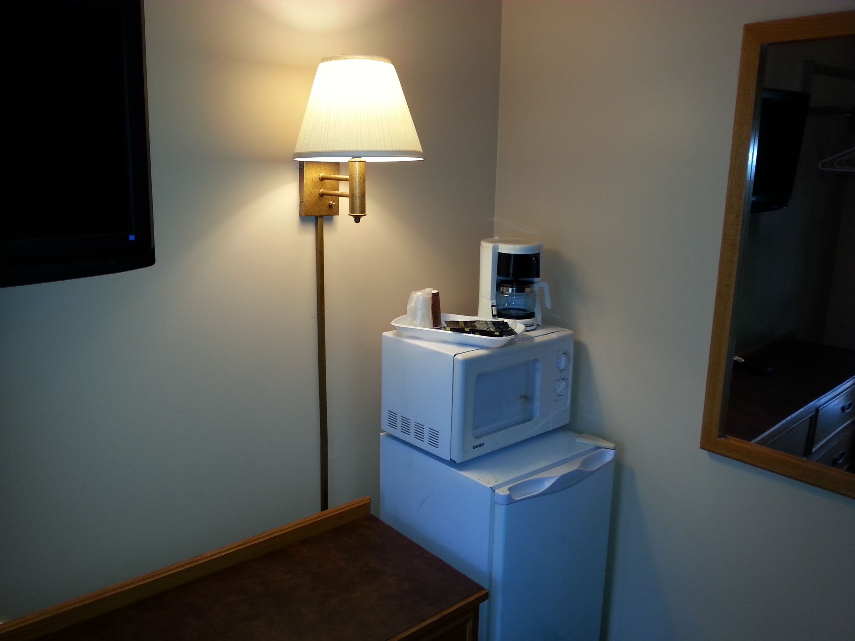Habitación de hotel compacta con microondas, cafetera y lámpara de pared.