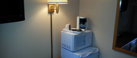 Habitación de hotel compacta con microondas, cafetera y lámpara de pared.