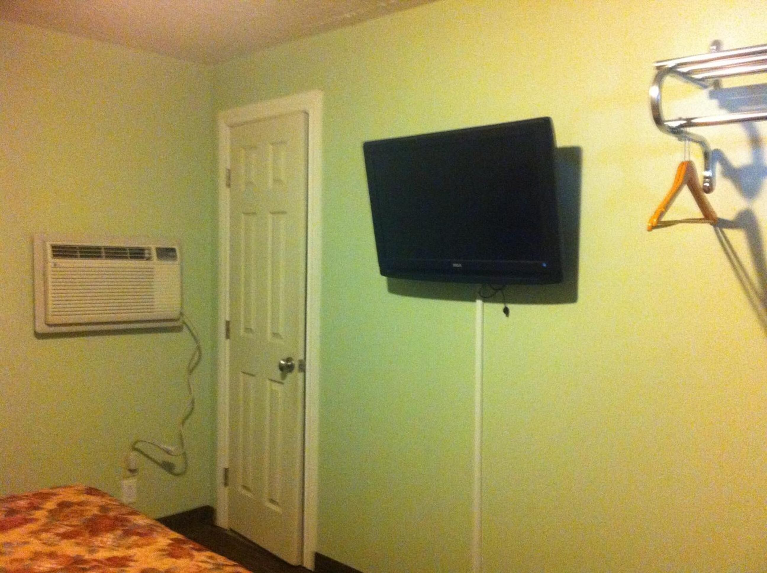 A room with a bed, an air conditioning unit, a closed door, and a mounted television.