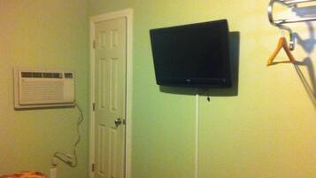 A room with a bed, an air conditioning unit, a closed door, and a mounted television.