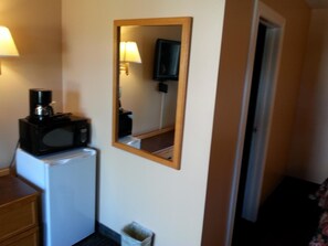 A hotel room with a microwave on a small refrigerator, a trash bin, and a mirror on the wall.