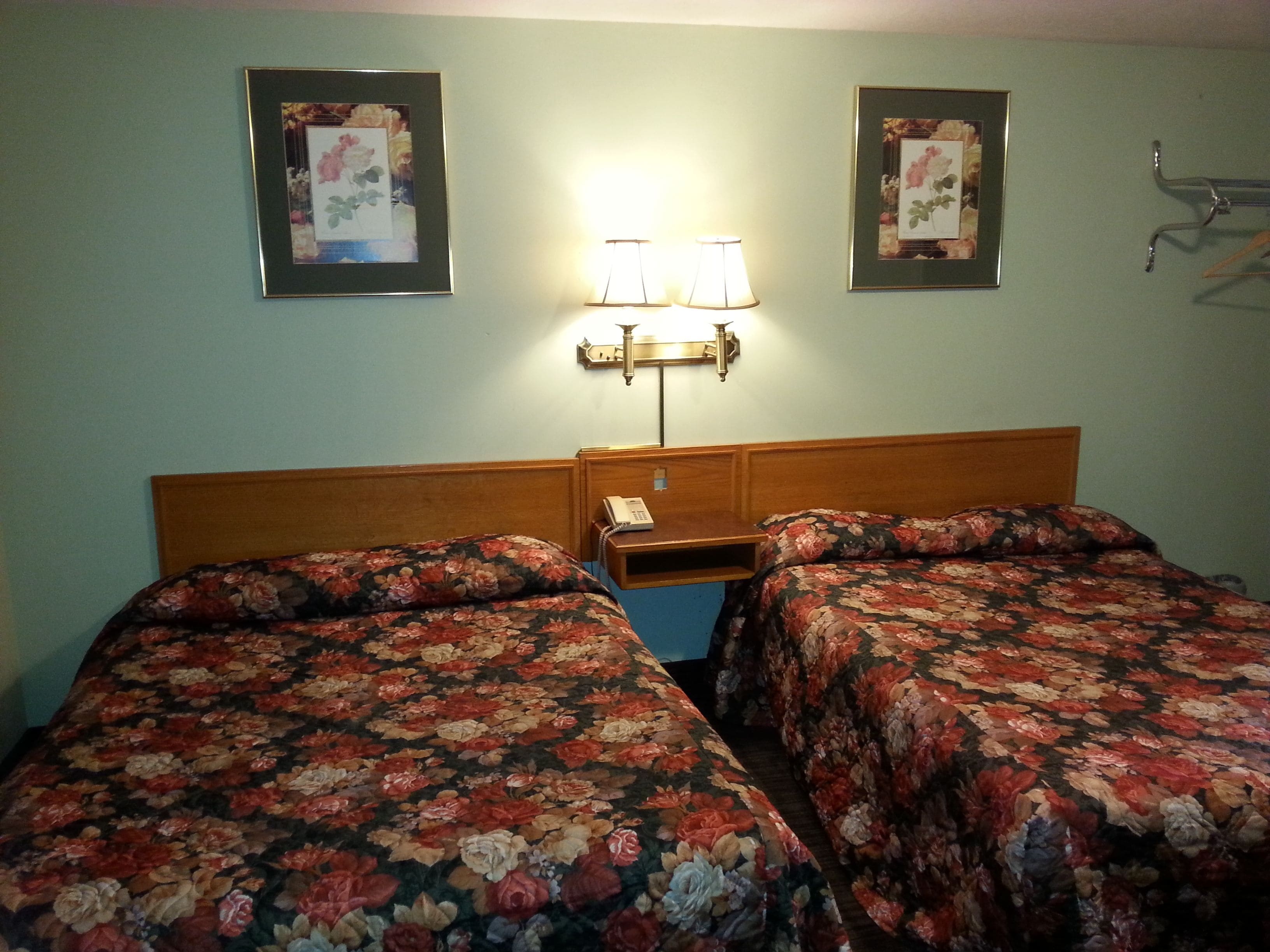 Een hotelkamer met twee bedden, een nachtkastje, een lamp en twee ingelijste bloemstillevens aan de muur.