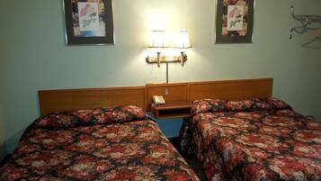 Een hotelkamer met twee bedden, een nachtkastje, een lamp en twee ingelijste bloemstillevens aan de muur.