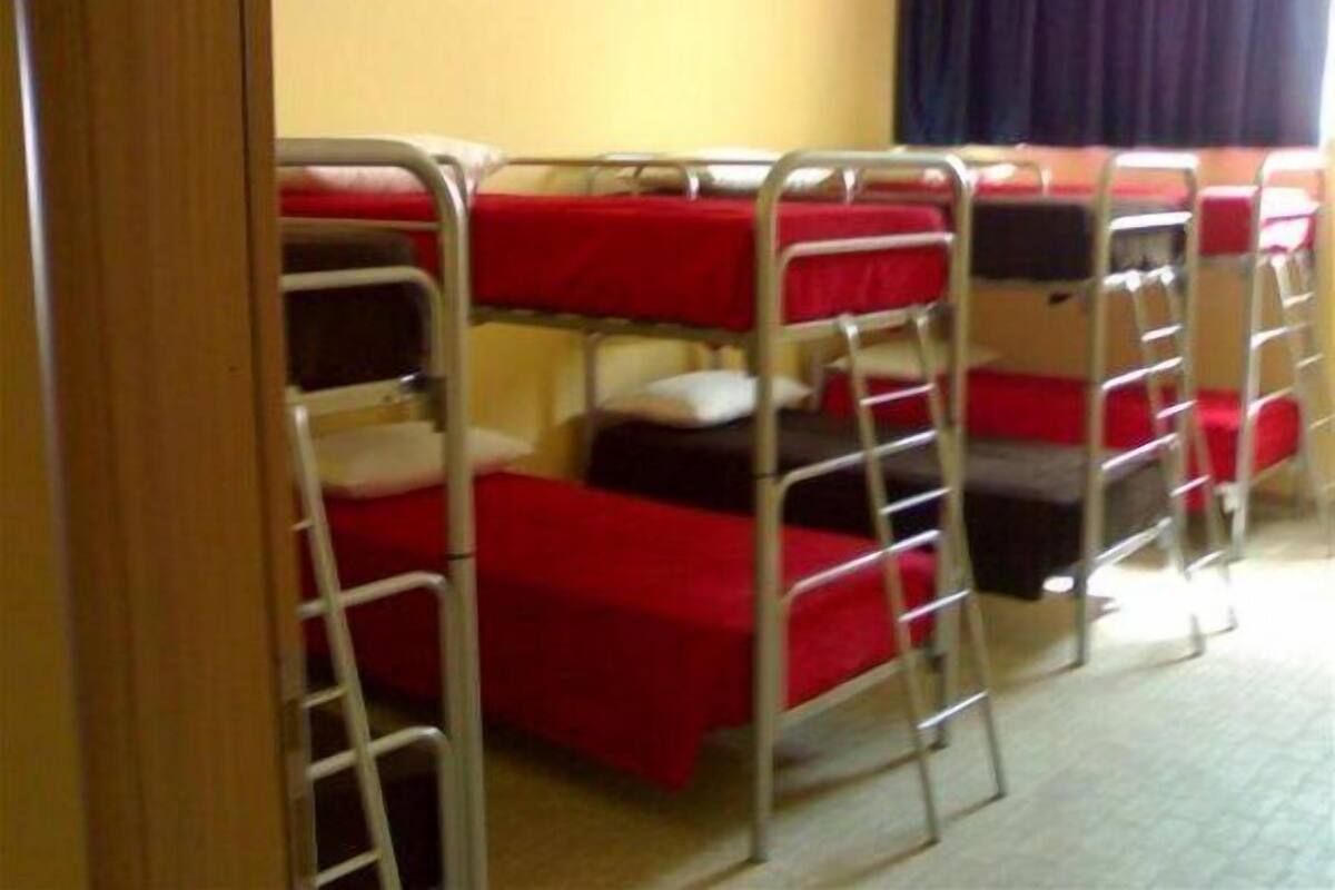 Camas literas con ropa de cama roja en una habitación con una puerta de madera y una cortina.