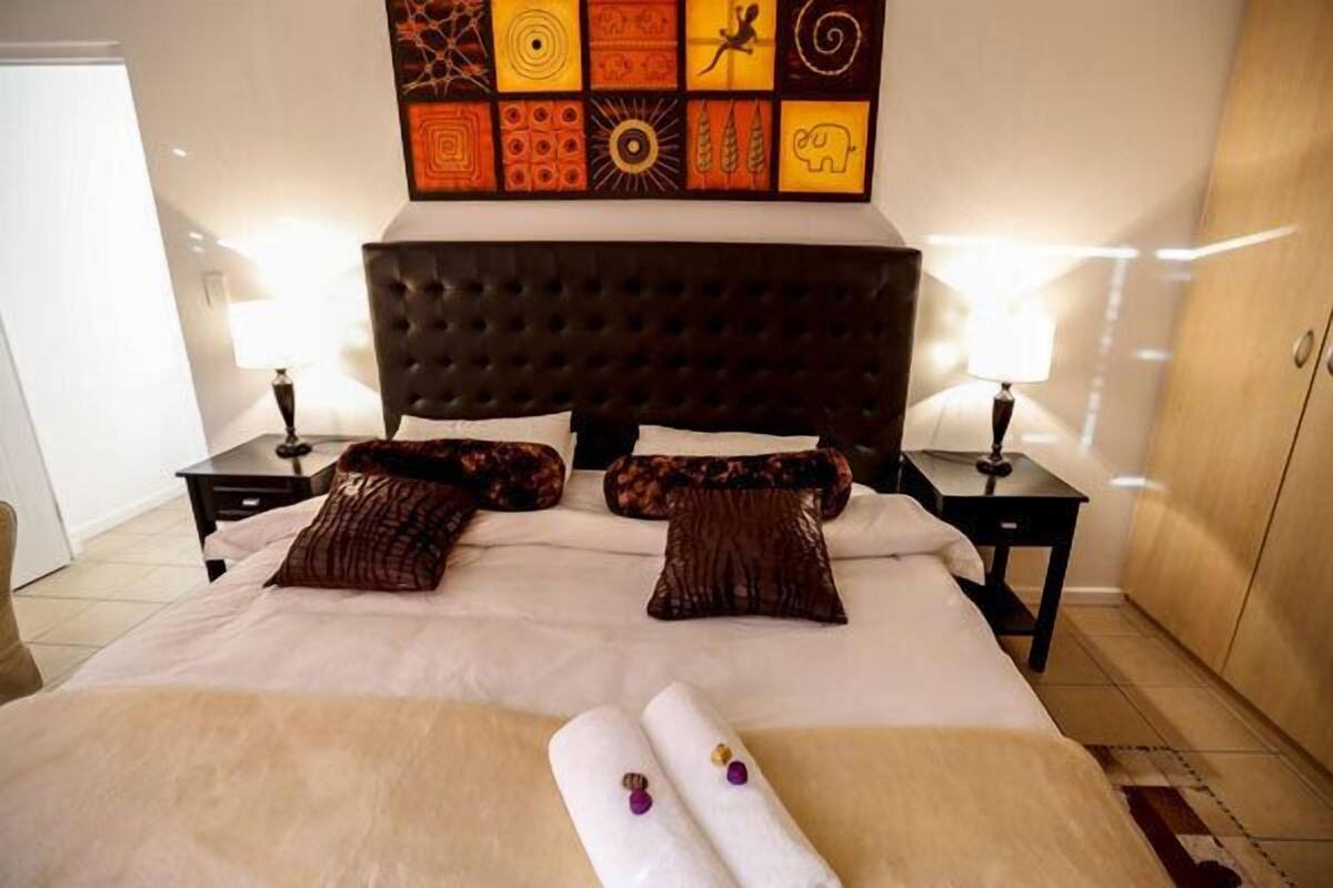 Habitación de hotel con una cama grande, cabecera oscura y una pared decorada con arte colorido. Hay dos mesitas de noche con lámparas.