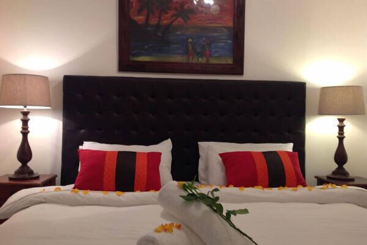 Habitación de hotel con una cama grande, dos almohadas, un cuadro en la pared y dos lámparas de noche.