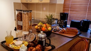 Una encimera de cocina con alimentos para el desayuno, como frutas, pan y equipo para preparar café.
