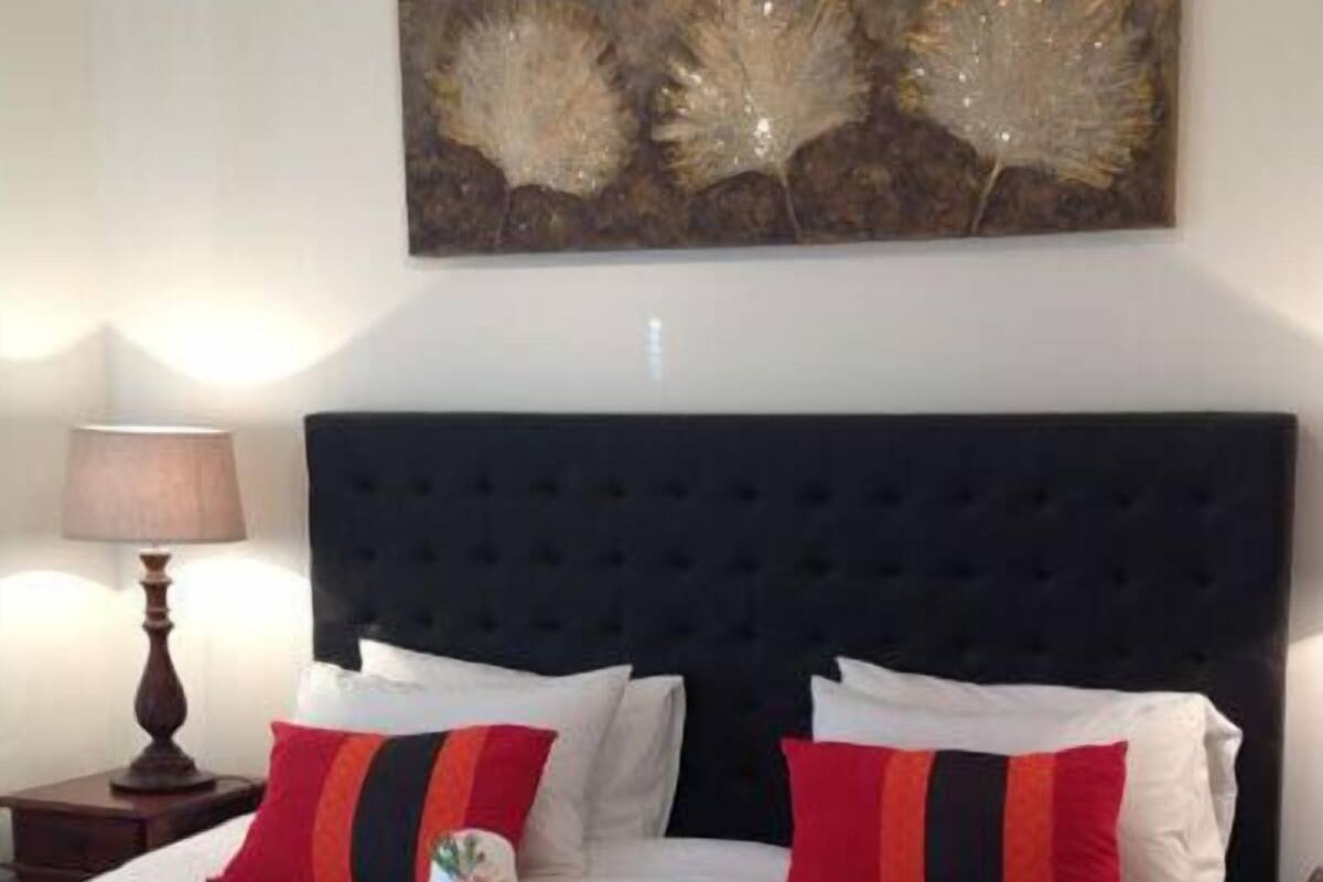 Una cama bien hecha con almohadas blancas y rojas, un cabecero oscuro y una obra de arte colgada en la pared.