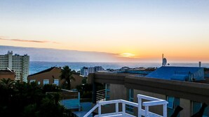 Un paisaje urbano costero al atardecer con edificios, cielo despejado y el océano al fondo.